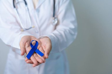 March Colectal Kanser Farkındalığı Ayı. Koyu mavi kurdeleli bir doktor. Yaşayan ve hastalıklı insanları destekliyor. Sağlık, umut ve Dünya Kanser Günü konsepti