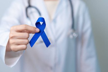 March Colectal Kanser Farkındalığı Ayı. Koyu mavi kurdeleli bir doktor. Yaşayan ve hastalıklı insanları destekliyor. Sağlık, umut ve Dünya Kanser Günü konsepti