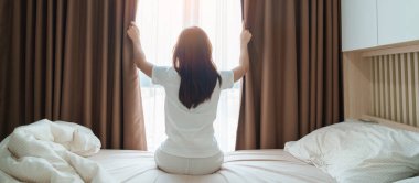 Mutlu kadın uyandıktan sonra yatağa uzanıyor, genç yetişkin kadın kollarını kaldırıyor ve sabahın erken saatlerinde pencereye bakıyor. Rahatlayın ve güzel bir gün geçirin.