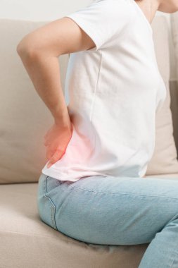 Evdeki koltukta otururken sırt ağrısı çeken bir kadın. Piriforis Sendromu, bel ağrısı ve omurga baskısı nedeniyle kas ağrısı olan yetişkin bir kadın. Ofis sendromu ve tıbbi konsept