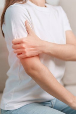 Evdeki koltukta otururken kolu ağrıyan bir kadın, kas hasarı ve ağrısı. Sağlık ve Tıp Konsepti