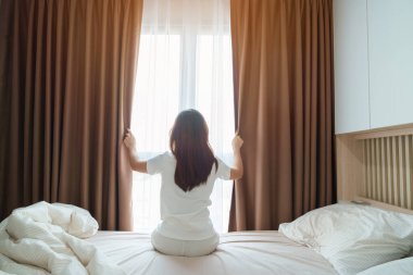 Mutlu kadın uyandıktan sonra yatağa uzanıyor, genç yetişkin kadın kollarını kaldırıyor ve sabahın erken saatlerinde pencereye bakıyor. Rahatlayın ve güzel bir gün geçirin.