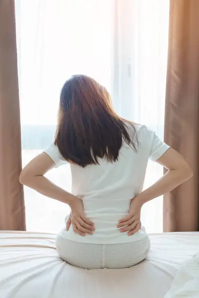 woman having back body ache during sitting on bed at home. adult female with muscle pain after Waking up due to Piriformis Syndrome, Low Back Pain and Spinal Compression. Health medical concept