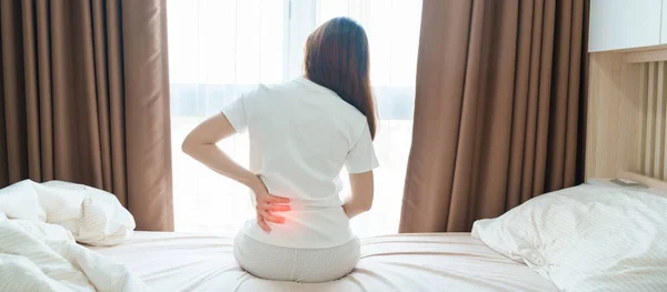 Frau Die Rückenschmerzen Hat Während Sie Hause Bett Sitzt Erwachsene lizenzfreie Stockbilder