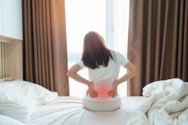 Evde yatakta otururken sırtı ağrıyan bir kadın. Piriforis Sendromu, Düşük Sırt Ağrısı ve Omurga Baskısı nedeniyle uyandıktan sonra kas ağrısı çeken yetişkin bir kadın. Sağlık Medikal Konsepti
