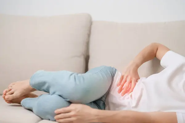 Woman having abdomen pain on the sofa at home. Liver cancer and Tumor, kidney cancer, Jaundice, Viral Hepatitis, Cirrhosis, Failure, Enlarged, Hepatic Encephalopathy, Stomach and health concept