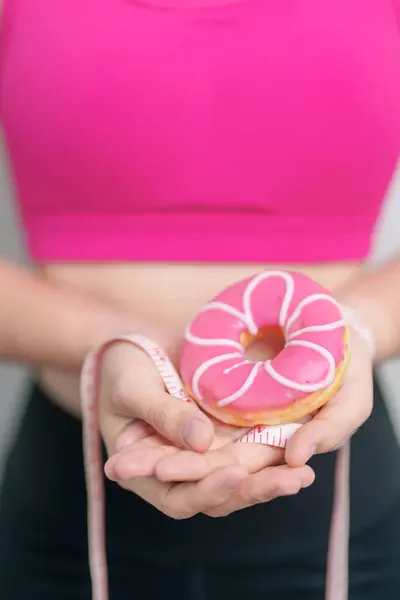 woman hand hold Donut with tape measure, choose stop eating sweet is Unhealthy ealthy food. Dieting control, Weight loss, Obesity, eating lifestyle and nutrition concepts