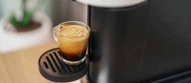 Kahve yaparken buharlı ve köpüklü Espresso bardağı. Kahve makinesinin yaptığı kahve, ahşap masa tezgahında. Kafe, günlük içecek içeceği Ev, Daire ve Ofis konsepti