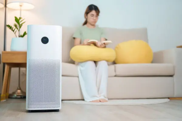 stock image Air Purifier with woman read and relax on sofa. Purification system for filter and cleaning dust PM2.5 HEPA and virus in home. Allergy, Pure air, health lifestyle, Wellness life and Air Pollution