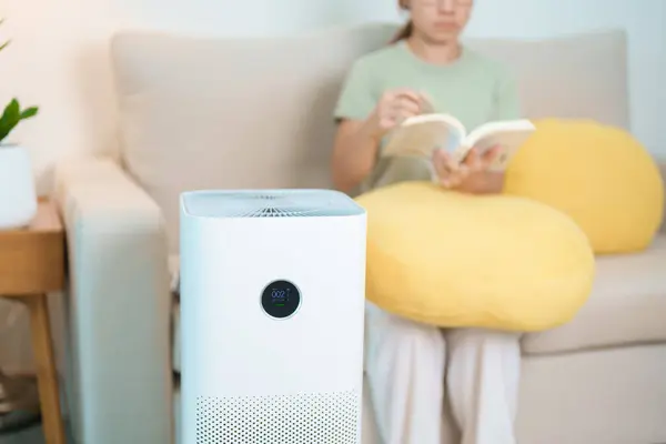 stock image Air Purifier with woman read and relax on sofa. Purification system for filter and cleaning dust PM2.5 HEPA and virus in home. Allergy, Pure air, health lifestyle, Wellness life and Air Pollution