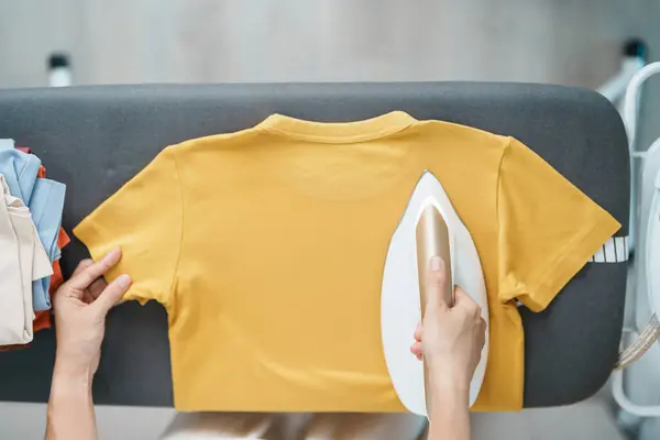 Woman hold Electric hot iron press T shirt clothes on ironing board, Intelligent automatic steam iron. Laundry, Housework, Housekeeping, Domestic hygiene, household of chores and daily routine concept