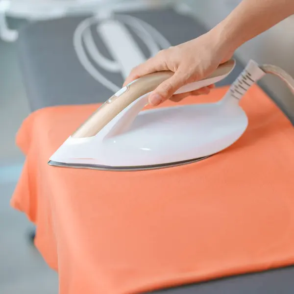 Woman hold Electric hot iron press T shirt clothes on ironing board, Intelligent automatic steam iron. Laundry, Housework, Housekeeping, Domestic hygiene, household of chores and daily routine concept