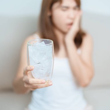 Dişler Soğuğa Duyarlı konsepti. Kadın elinde buzlu su bardağı ile yemekten sonra diş ağrısı ve ağrı çekiyor. Diş çürüğü veya Sakız Hastalığı, Öğütücü Diş ve Stres, Korunmasız Sinir Kökleri, Çatlak ve Alınan Dişetleri