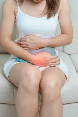 Aylık ve mide ağrısı konseptlerinin adet döngüsü. Karın ağrısı çeken bir kadın, sıcak su şişesi ile adet sancısı çeken bir kadın, regl öncesi ağrı çeken bir kadın ve vücut sağlığı problemi olan bir kadın.