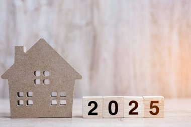 2025 Mutlu Yıllar, masa başı ahşap arka planda ev modeliyle. Bankacılık, gayrimenkul, yatırım, finans, tasarruf ve yeni yıl kararı kavramları