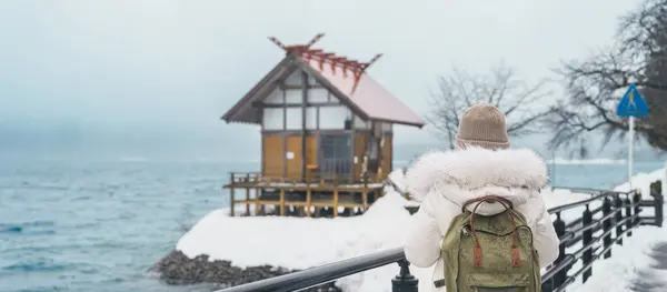 stock image Woman tourist sightseeing Kansa Shrine and Lake Tazawa in winter. Traveler travel in Semboku city, Akita Prefecture, Japan. Landmark for tourist attraction in Tohoku region. Japan travel and vacation