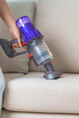 Kablosuz elektrik süpürgesiyle kanepeyi temizleyen kadın. Ev hanımı kablosuz süpürgeyi evi temizlemek için kullanıyor. Ev işleri, Temizlik, Temizlik, Temizlik, Toz, Temizlik ve günlük rutin