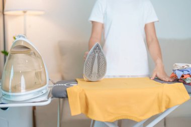 Kadın ütü masasında elektrikli ütü ütülü tişört, akıllı otomatik buhar ütüsü tutuyor. Çamaşır, ev işleri, temizlik, ev temizliği, ev işleri ve günlük rutin konsept.