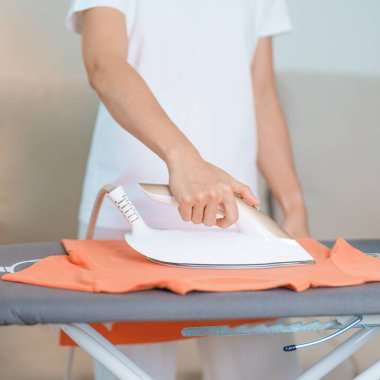 Kadın ütü masasında elektrikli ütü ütülü tişört, akıllı otomatik buhar ütüsü tutuyor. Çamaşır, ev işleri, temizlik, ev temizliği, ev işleri ve günlük rutin konsept.