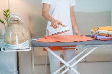 Kadın ütü masasında elektrikli ütü ütülü tişört, akıllı otomatik buhar ütüsü tutuyor. Çamaşır, ev işleri, temizlik, ev temizliği, ev işleri ve günlük rutin konsept.