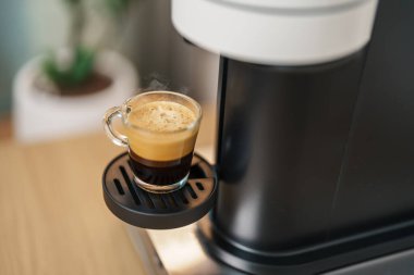 Kahve yaparken buharlı ve köpüklü Espresso bardağı. Kahve makinesinin yaptığı kahve, ahşap masa tezgahında. Kafe, günlük içecek içeceği Ev, Daire ve Ofis konsepti