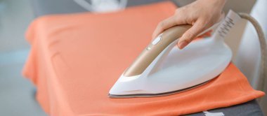 Kadın ütü masasında elektrikli ütü ütülü tişört, akıllı otomatik buhar ütüsü tutuyor. Çamaşır, ev işleri, temizlik, ev temizliği, ev işleri ve günlük rutin konsept.