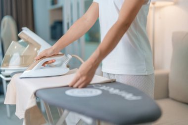 Kadın ütü masasında elektrikli ütü ütülü tişört, akıllı otomatik buhar ütüsü tutuyor. Çamaşır, ev işleri, temizlik, ev temizliği, ev işleri ve günlük rutin konsept.