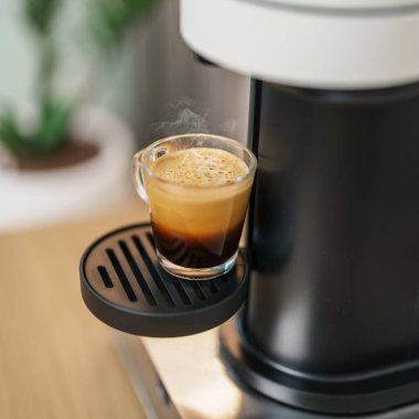 Kahve yaparken buharlı ve köpüklü Espresso bardağı. Kahve makinesinin yaptığı kahve, ahşap masa tezgahında. Kafe, günlük içecek içeceği Ev, Daire ve Ofis konsepti