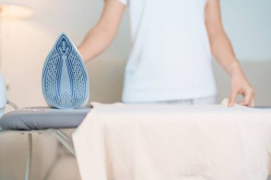 Kadın ütü masasında elektrikli ütü ütülü tişört, akıllı otomatik buhar ütüsü tutuyor. Çamaşır, ev işleri, temizlik, ev temizliği, ev işleri ve günlük rutin konsept.