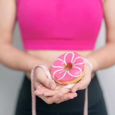 Kadın elinde mezurayla donut tutuyor, tatlı yemeyi bırakmayı seçiyor sağlıksız yiyecekler. Diyet kontrolü, kilo kaybı, obezite, yeme tarzı ve beslenme kavramları