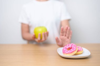 Kadın ellerinin yeşil elma tutması ve çöreği reddetmesi, kadın fitness seçimiyle meyve sağlıklı ve tatlı, sağlıksız abur cuburdur. Diyet kontrolü, kilo kaybı, obezite, yeme tarzı ve beslenme