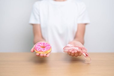 Kadın elinde mezurayla donut tutuyor, tatlı yemeyi bırakmayı seçiyor sağlıksız yiyecekler. Diyet kontrolü, kilo kaybı, obezite, yeme tarzı ve beslenme kavramları