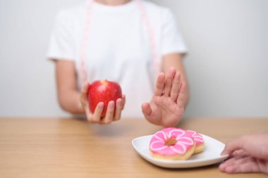 Kadın eli kırmızı elma tutuyor ve donutu reddediyor, kadın spor salonu meyvelerle sağlıklı ve tatlı sağlıklı olmayan abur cuburlar arasında seçim yapıyor. Diyet kontrolü, kilo kaybı, obezite, yeme tarzı ve beslenme