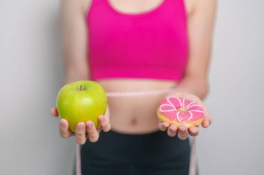 Kadın elini yeşil elma ve çörek ile tutar, kadın fitness meyve ve tatlı sağlıklı ve sağlıksız abur cubur arasında seçim yapar. Diyet kontrolü, kilo kaybı, obezite, yeme tarzı ve beslenme konsepti