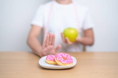 Kadın ellerinin yeşil elma tutması ve çöreği reddetmesi, kadın fitness seçimiyle meyve sağlıklı ve tatlı, sağlıksız abur cuburdur. Diyet kontrolü, kilo kaybı, obezite, yeme tarzı ve beslenme