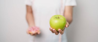 Kadın elini yeşil elma ve çörek ile tutar, kadın fitness meyve ve tatlı sağlıklı ve sağlıksız abur cubur arasında seçim yapar. Diyet kontrolü, kilo kaybı, obezite, yeme tarzı ve beslenme konsepti
