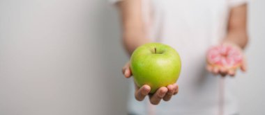 Kadın elini yeşil elma ve çörek ile tutar, kadın fitness meyve ve tatlı sağlıklı ve sağlıksız abur cubur arasında seçim yapar. Diyet kontrolü, kilo kaybı, obezite, yeme tarzı ve beslenme konsepti