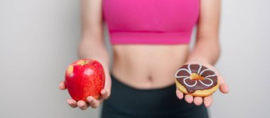 Kadın eldiveni kırmızı elma ve çörek, kadın spor salonu meyve ve tatlı sağlıklı ve sağlıksız abur cuburdur. Diyet kontrolü, kilo kaybı, obezite, yeme tarzı ve beslenme konsepti