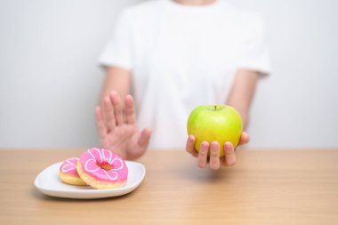 Kadın ellerinin yeşil elma tutması ve çöreği reddetmesi, kadın fitness seçimiyle meyve sağlıklı ve tatlı, sağlıksız abur cuburdur. Diyet kontrolü, kilo kaybı, obezite, yeme tarzı ve beslenme
