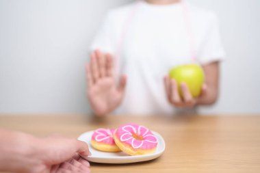 Kadın ellerinin yeşil elma tutması ve çöreği reddetmesi, kadın fitness seçimiyle meyve sağlıklı ve tatlı, sağlıksız abur cuburdur. Diyet kontrolü, kilo kaybı, obezite, yeme tarzı ve beslenme