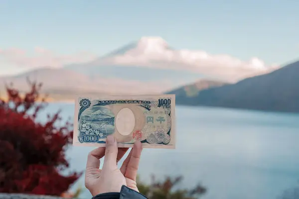 stock image Hand holding 1000 yen banknote with mount Fuji at Lake Motosu, happy tourist travel Mt Fuji and road trip Fuji Five Lakes. Landmark for tourists attraction. Japan Travel, Destination and Vacation