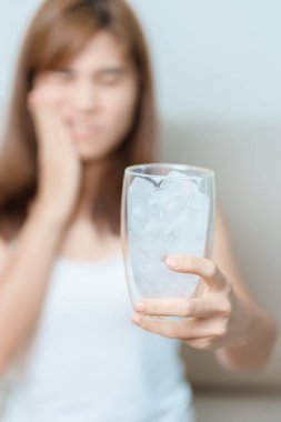 Dişler Soğuğa Duyarlı konsepti. Kadın elinde buzlu su bardağı ile yemekten sonra diş ağrısı ve ağrı çekiyor. Diş çürüğü veya Sakız Hastalığı, Öğütücü Diş ve Stres, Korunmasız Sinir Kökleri, Çatlak ve Alınan Dişetleri