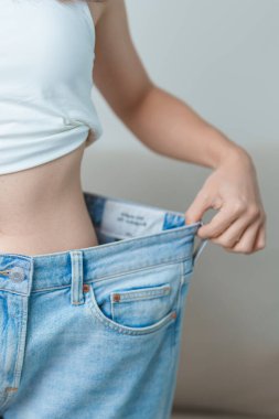 Genç, zayıf bir kadın, büyük ya da büyük beden kot pantolon giyiyor, kadın kilo verdikten sonra sağlıklı görünüyor. diyet, egzersiz, vücut fit ve yağ aldırma ameliyatı konsepti