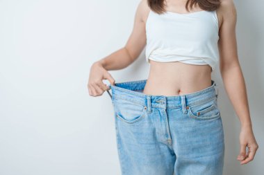Genç, zayıf bir kadın, büyük ya da büyük beden kot pantolon giyiyor, kadın kilo verdikten sonra sağlıklı görünüyor. diyet, egzersiz, vücut fit ve yağ aldırma ameliyatı konsepti