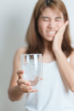 Dişler Soğuğa Duyarlı konsepti. Kadın elinde buzlu su bardağı ile yemekten sonra diş ağrısı ve ağrı çekiyor. Diş çürüğü veya Sakız Hastalığı, Öğütücü Diş ve Stres, Korunmasız Sinir Kökleri, Çatlak ve Alınan Dişetleri