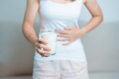 Laktoz intoleransı ve süt alerjisi konsepti. Kadın süt bardağı tutuyor ve karın krampları ve inek sütü içerken ağrı yapıyor. Semptom mide ağrısı, süt ürünlerine duyarlılık, mide bulantısı, şişkinlik, gaz ve ishal.