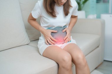 Aylık ve mide ağrısı konseptlerinin adet döngüsü. Karın ağrısı çeken bir kadın, sıcak su şişesi ile adet sancısı çeken bir kadın, regl öncesi ağrı çeken bir kadın ve vücut sağlığı problemi olan bir kadın.