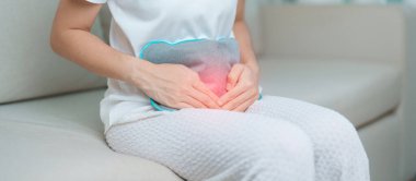 Aylık ve mide ağrısı konseptlerinin adet döngüsü. Karın ağrısı çeken bir kadın, sıcak su şişesi ile adet sancısı çeken bir kadın, regl öncesi ağrı çeken bir kadın ve vücut sağlığı problemi olan bir kadın.