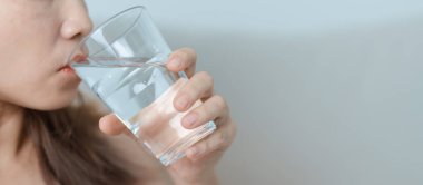 Su bardağı tutan mutlu kadın, evdeki kanepede saf su içen kadın. Sağlıklı, ferahlatıcı, yaşam tarzı ve günlük rutin konsept