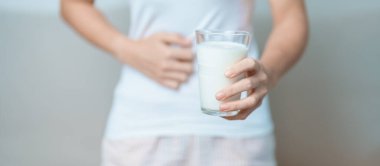 Laktoz intoleransı ve süt alerjisi konsepti. Kadın süt bardağı tutuyor ve karın krampları ve inek sütü içerken ağrı yapıyor. Semptom mide ağrısı, süt ürünlerine duyarlılık, mide bulantısı, şişkinlik, gaz ve ishal.